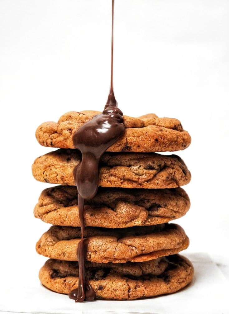 A stack of chocolate-chip cookies with warm chocolate drizzling down the side